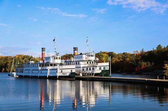 A white steamship docked on a Muskoka lake in autumn
